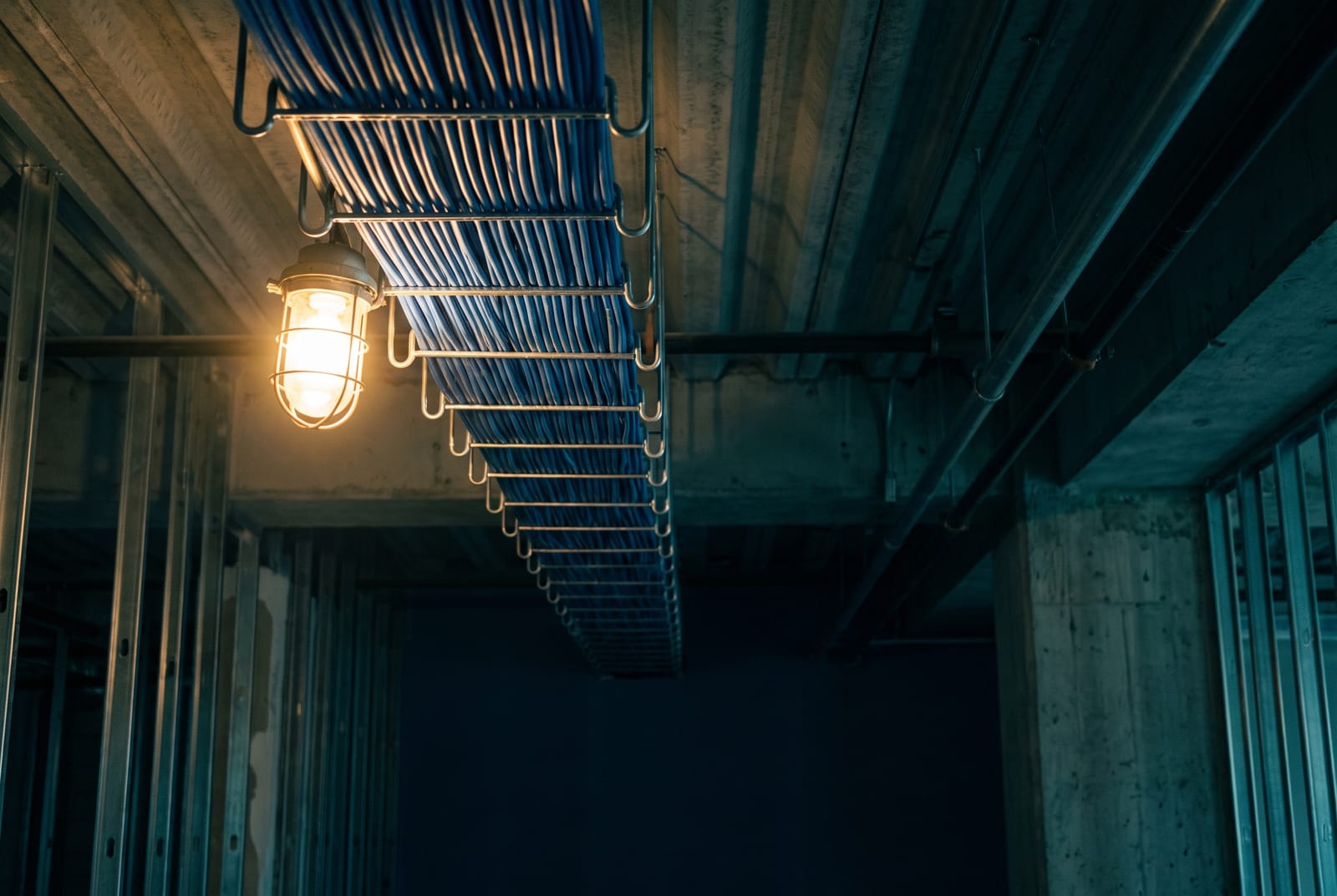 Neatly bundled blue Cat6 cable running along a J-hook pathway through a dark ceiling void